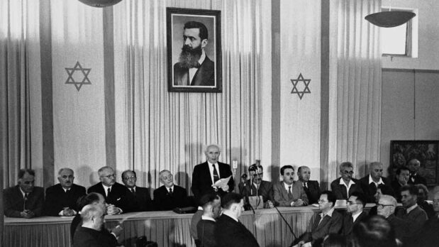 David Ben-Gurion publicly pronouncing the Declaration of the State of Israel on May 14, 1948, in Tel Aviv, beneath a large portrait of Theodor Herzl, the founder of modern political Zionism. (Public Domain)